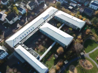 Schulgebäude von oben davor Wiese und Bäume